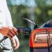 Person holding a charging connector beside an electric car’s open charging port